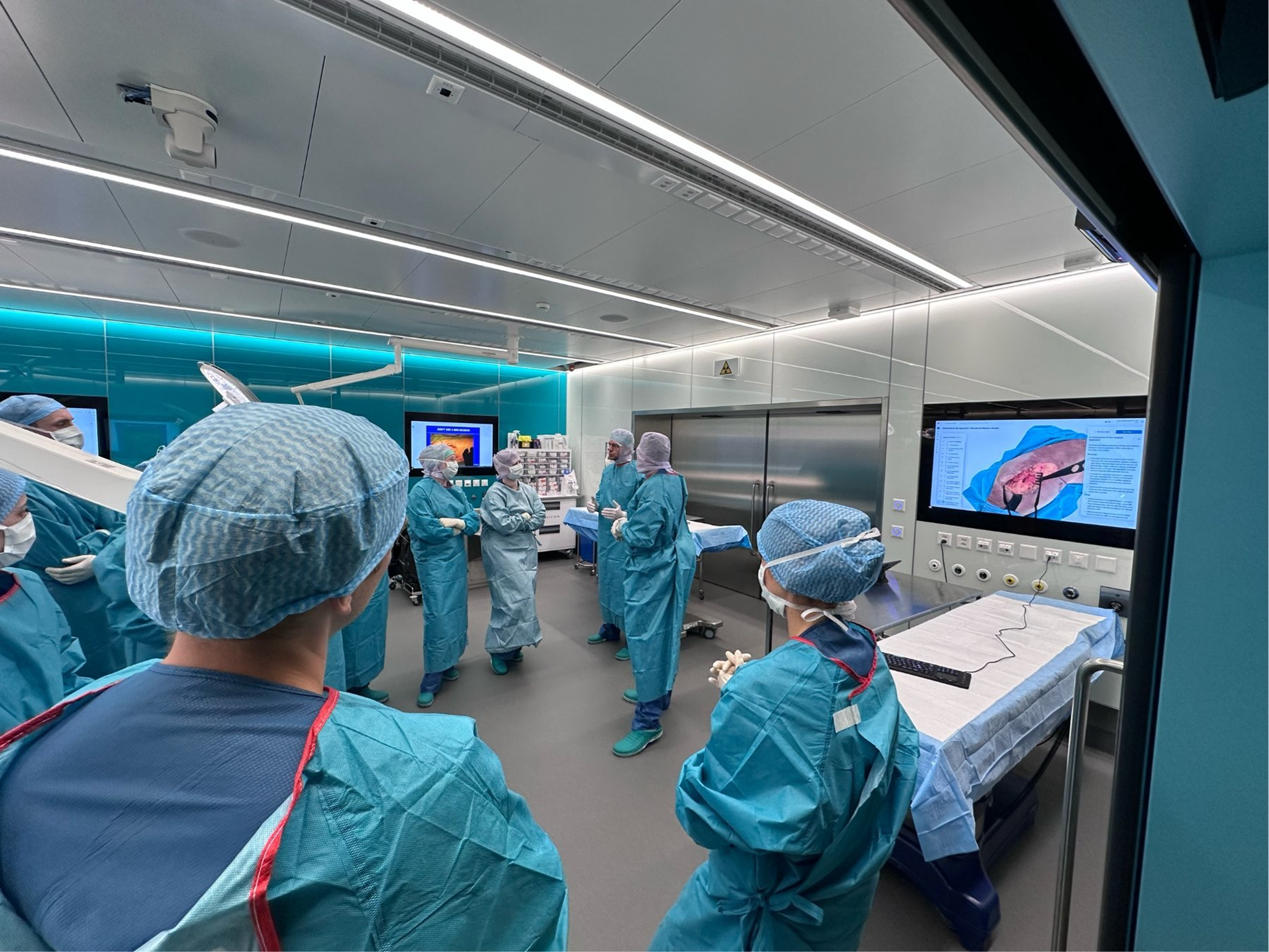 Trainees in surgical gowns during a hands-on teaching session at OR-X in Zurich, with an AUGMEDI approach module on the screen. 